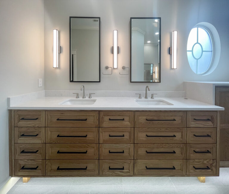 Custom white oak double vanity with extensive drawers, quartz countertops with under mount sinks, brushed nickel hardware, integrated under-cabinet lighting and black framed recessed medicine cabinets mirrors.