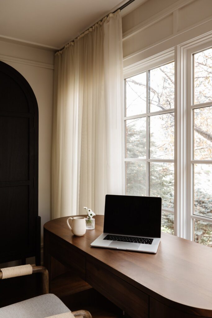 Laptop and a morning cup of coffee at wooden desk looking out a window