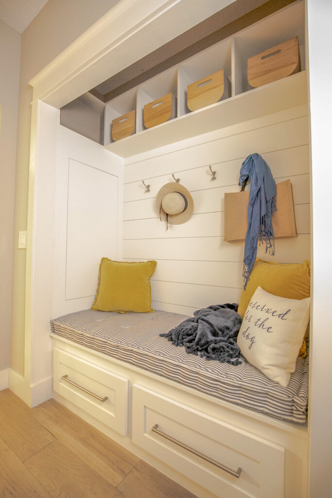 Built-in drop zone with blue and white striped cushion and yellow cushions, with hooks and baskets above.