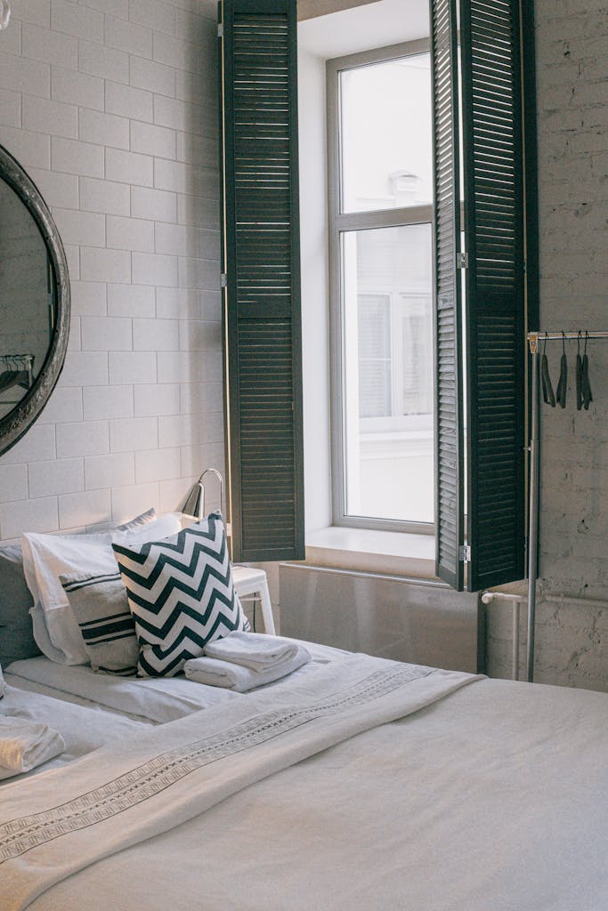 A cozy and stylish bedroom featuring modern decor and a sunlit window with shutter panels.