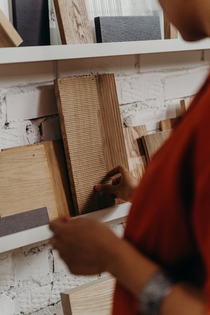Close-up of a person selecting wooden material samples from a display shelf against a brick wall.