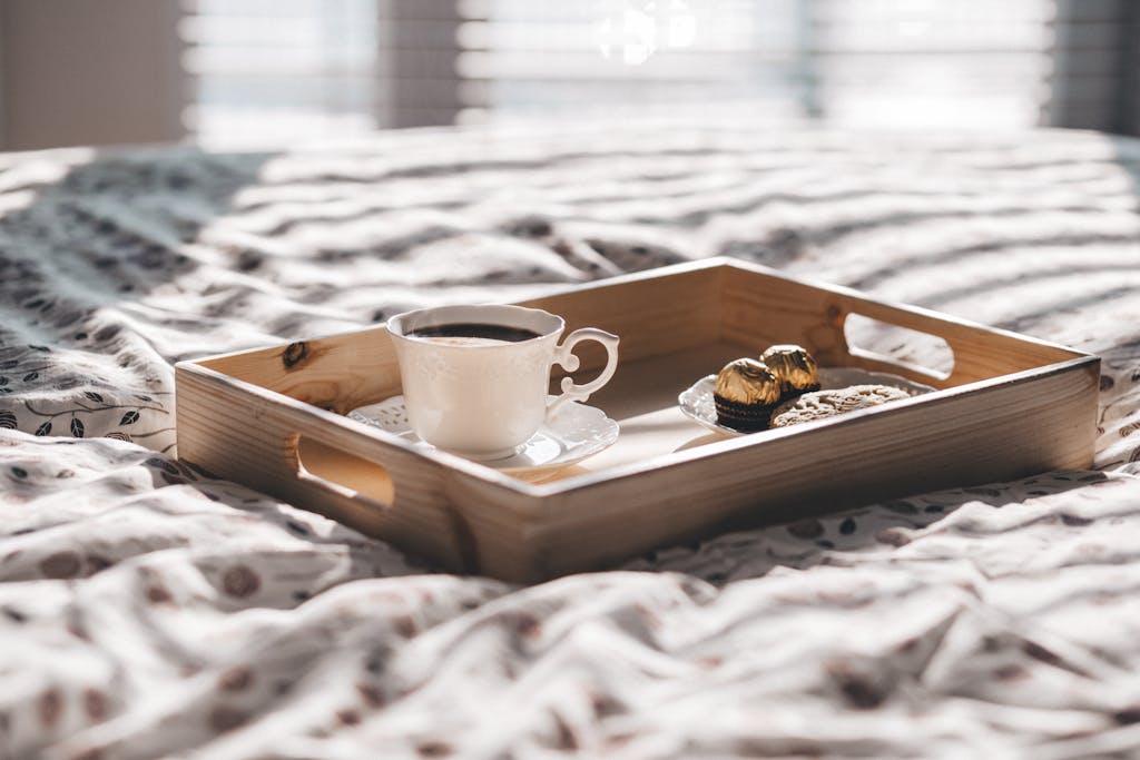 Elegant morning setup with coffee and chocolates on a wooden tray on bed.