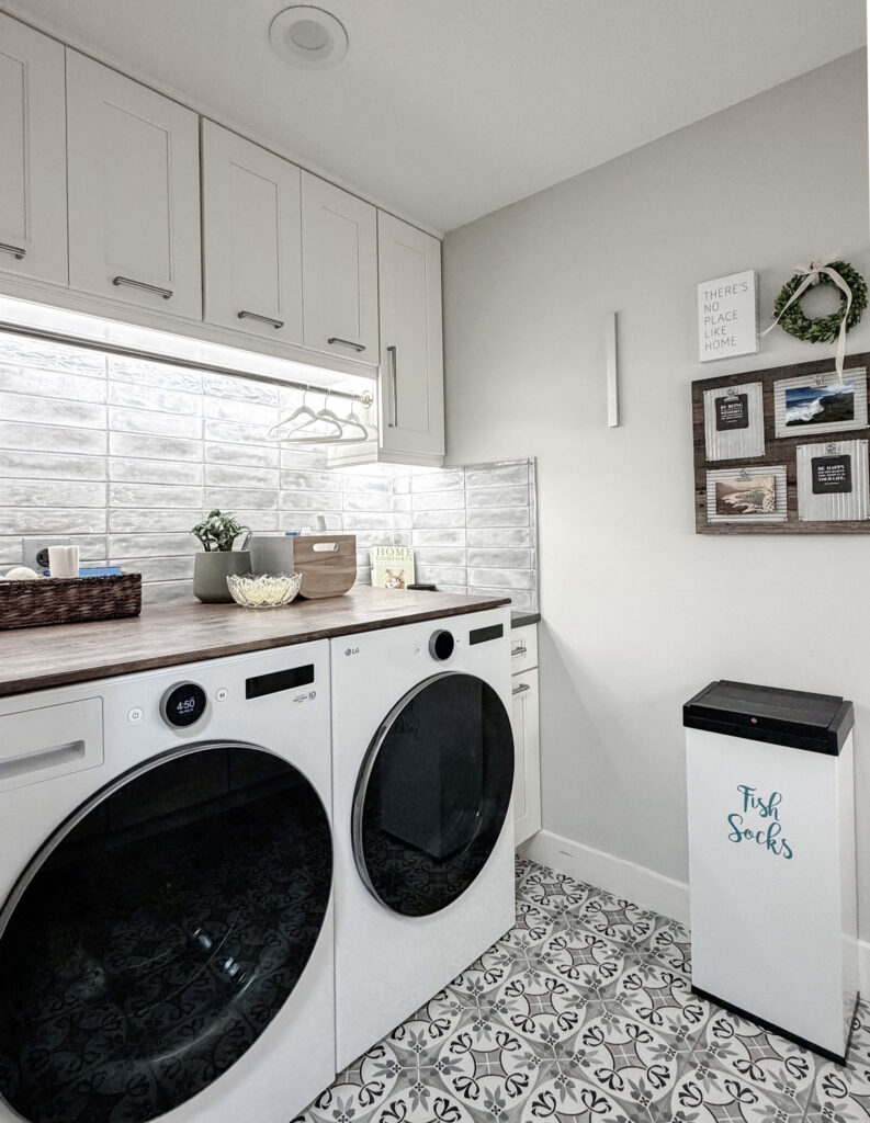 Laundry room after a renovation with washer and dryer, custom white cabinets, and utility sink with patterned tile floor, subway tile backsplash, and quartz countertops.