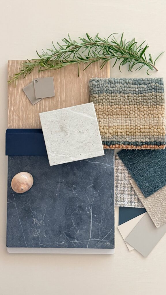 Interior design material palette with blue stone, creamy quartz, navy cabinetry, warm oak, layered textured fabrics, brushed nickel hardware, rosemary, and a shell.