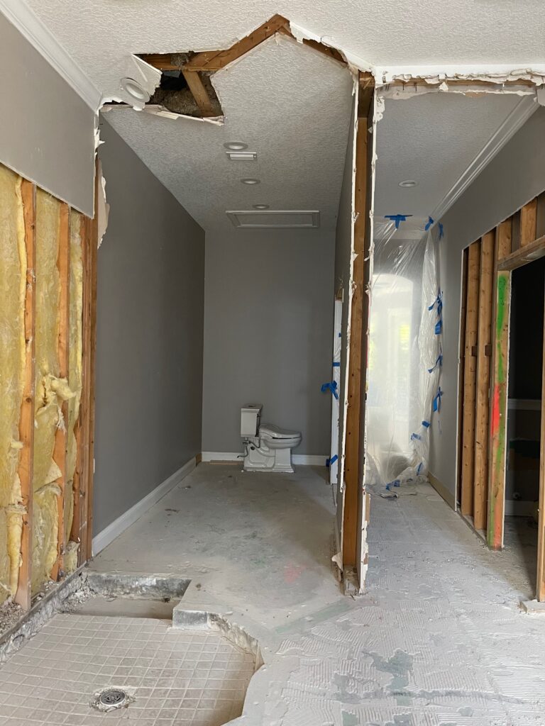 Primary bathroom during renovation with walls and slab concrete slab opened for plumbing relocation to support the redesigned shower layout.