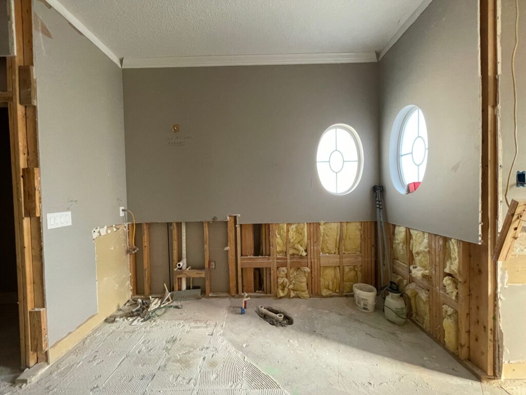 Demolition of the original primary bathroom showing exposed wall framing after removal of the built-in tub and surrounding finishes.